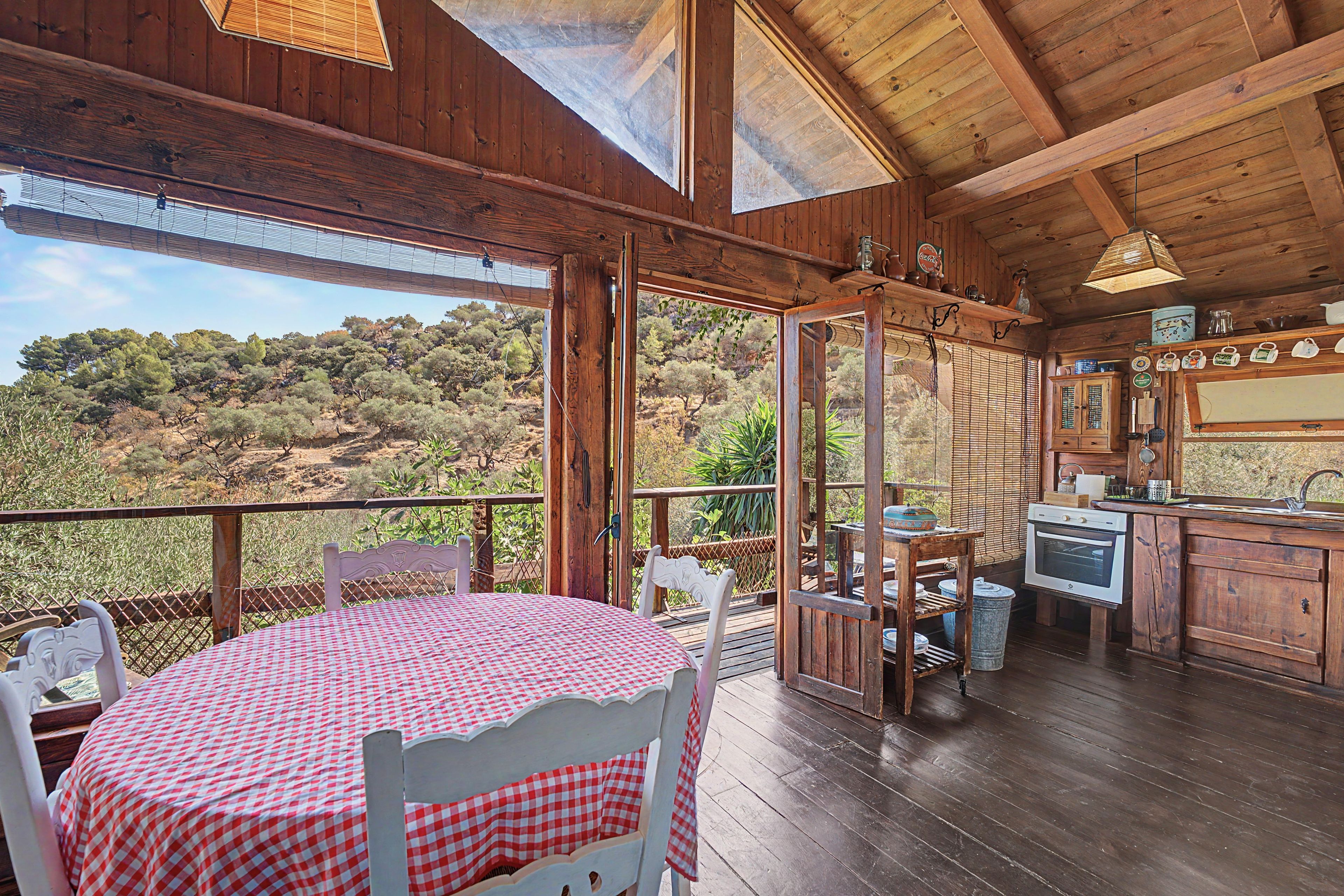 Une cabane en bois comprenant un coin repas, une cuisine et de grandes fenêtres donnant sur un paysage vallonné.