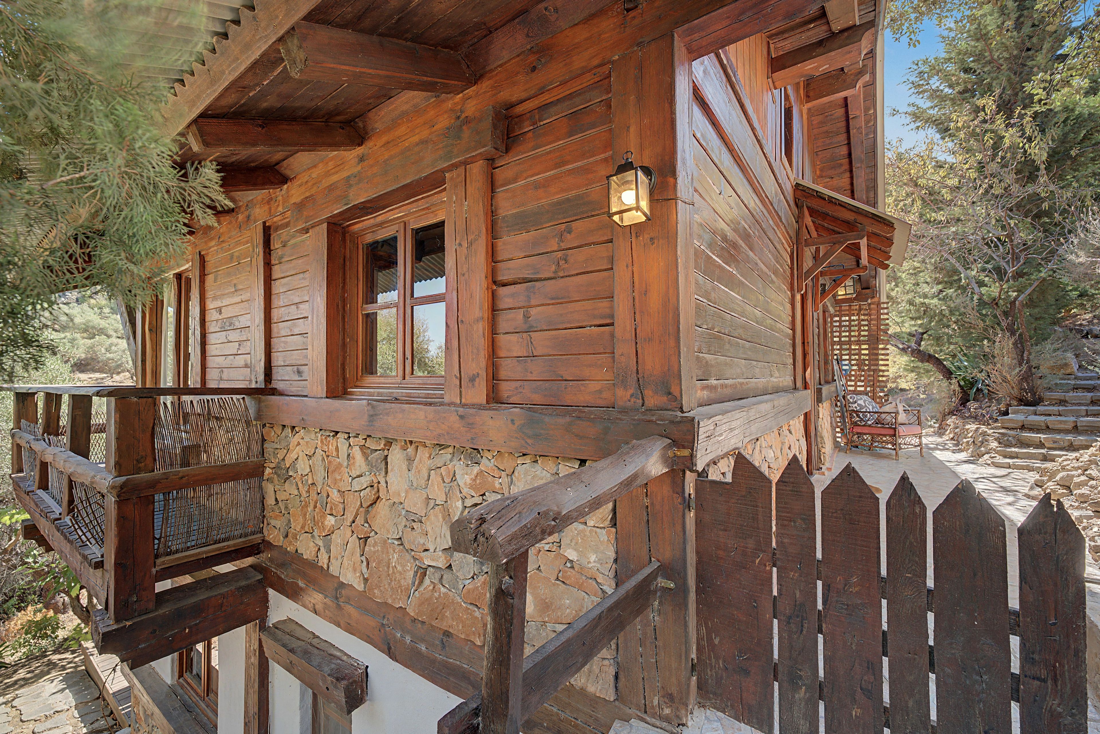 Eine Holzhütte mit Steinunterbau, einer Holzterrasse und einem Palisadenzaun.