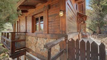 Eine Holzhütte mit Steinunterbau, einer Holzterrasse und einem Palisadenzaun.