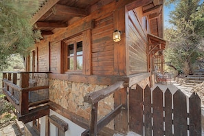 A wooden cabin with a stone foundation, a wooden deck, and a picket fence.