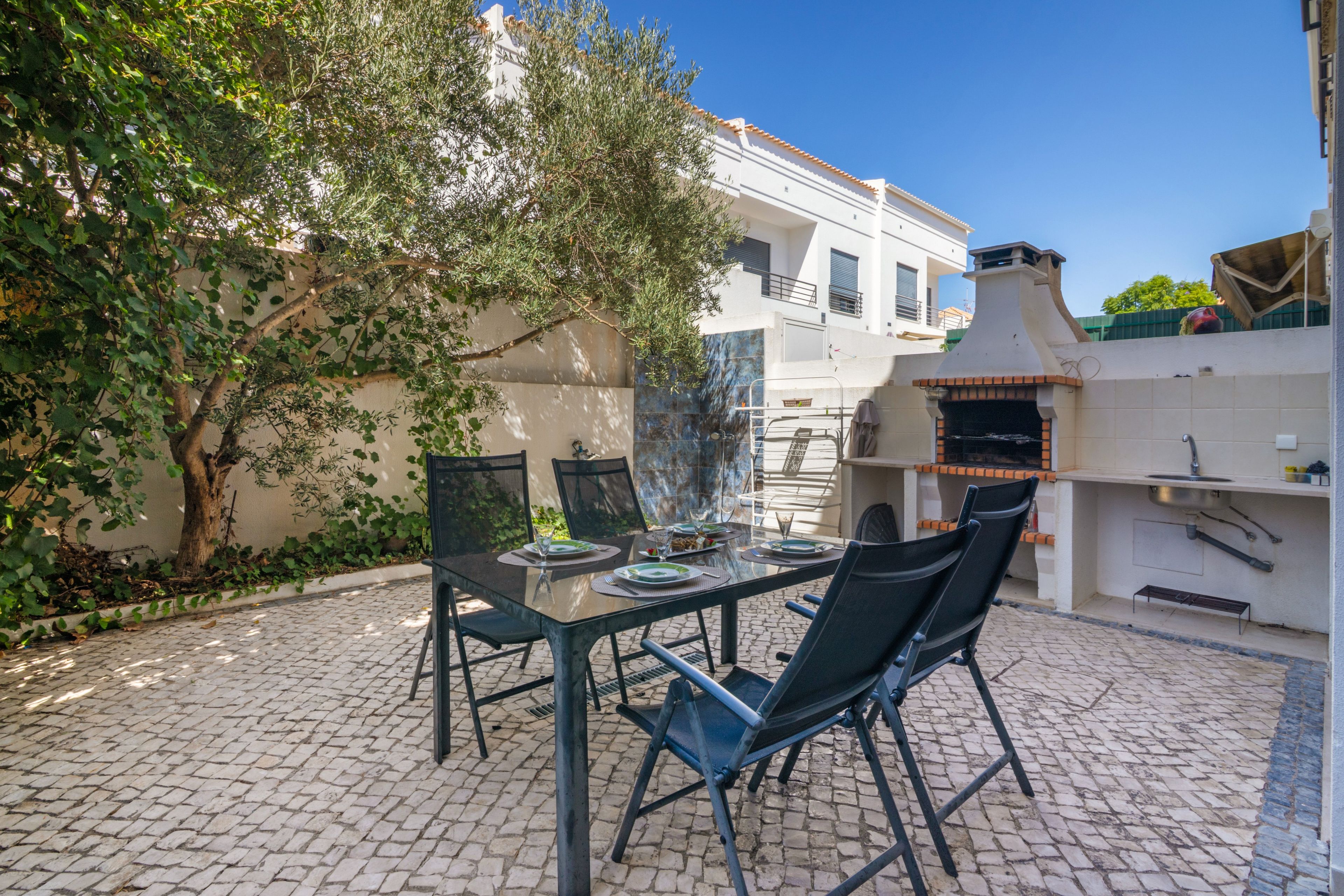 Un patio exterior con mesa lista para comer, rodeado de sillas y una zona de barbacoa.