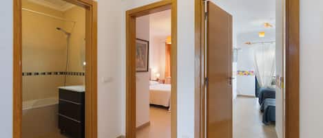 Un couloir d’hôtel donnant accès à une salle de bain, une chambre et un coin salon.