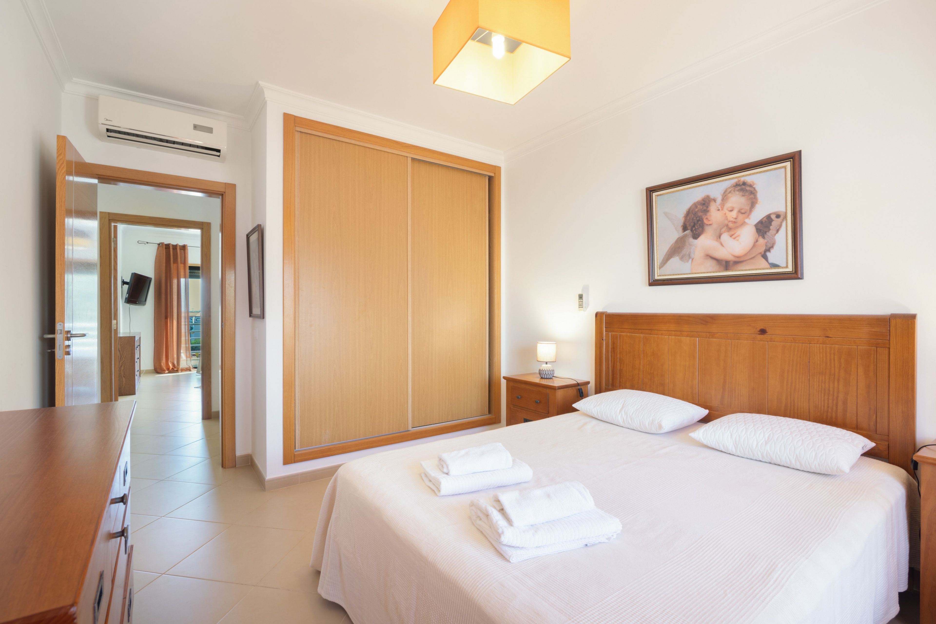 Ein Hotelzimmer mit Bett, Nachttisch, Nachttischlampe, Kleiderschrank und einem gerahmten Bild an der Wand.