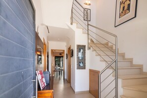 Un couloir mène à un escalier doté d’une rampe en métal, à un coin repas avec des chaises et une table, et une œuvre d’art encadrée orne le mur.