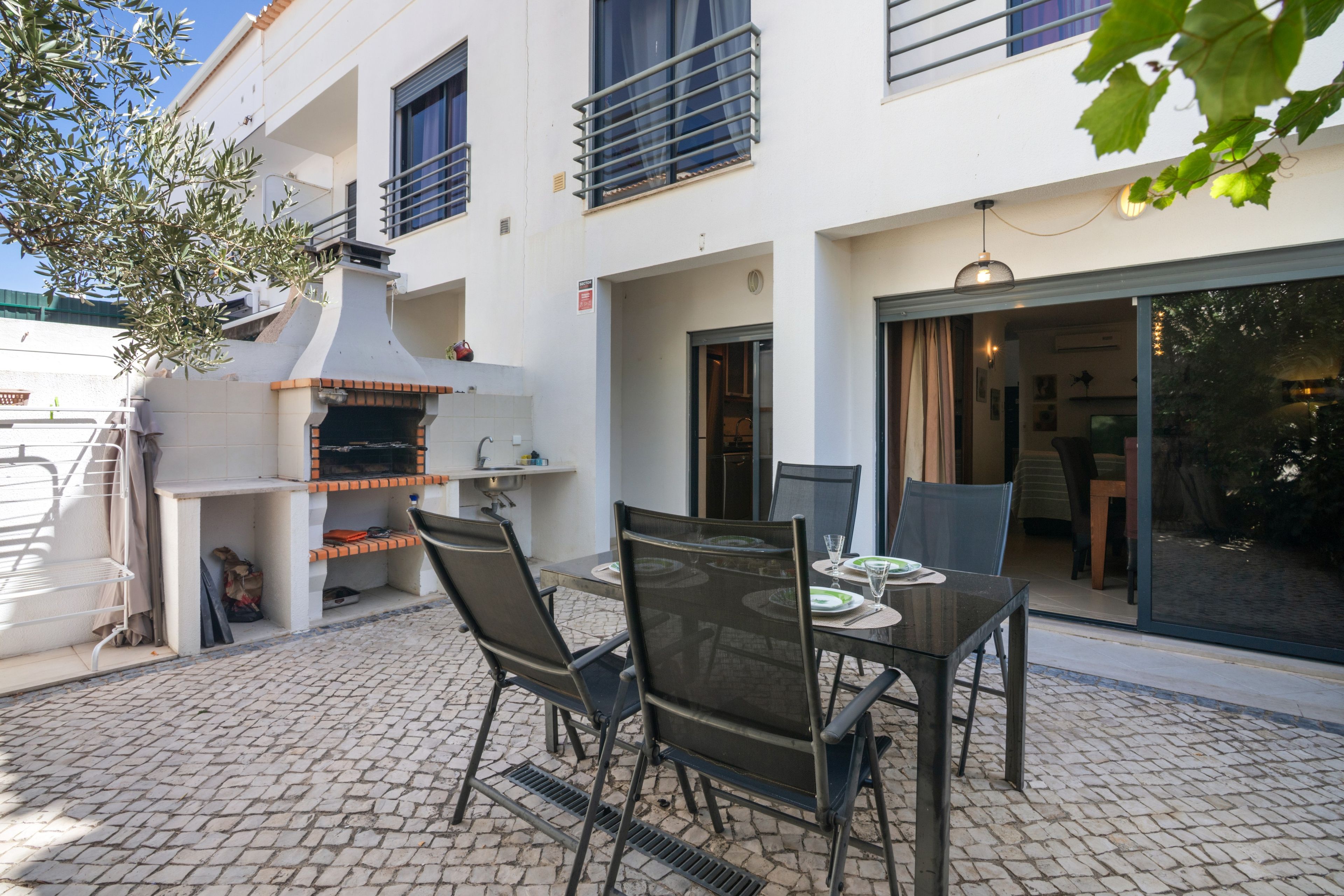 Un patio al aire libre con horno de ladrillo, mesa, sillas y vistas al interior del edificio.