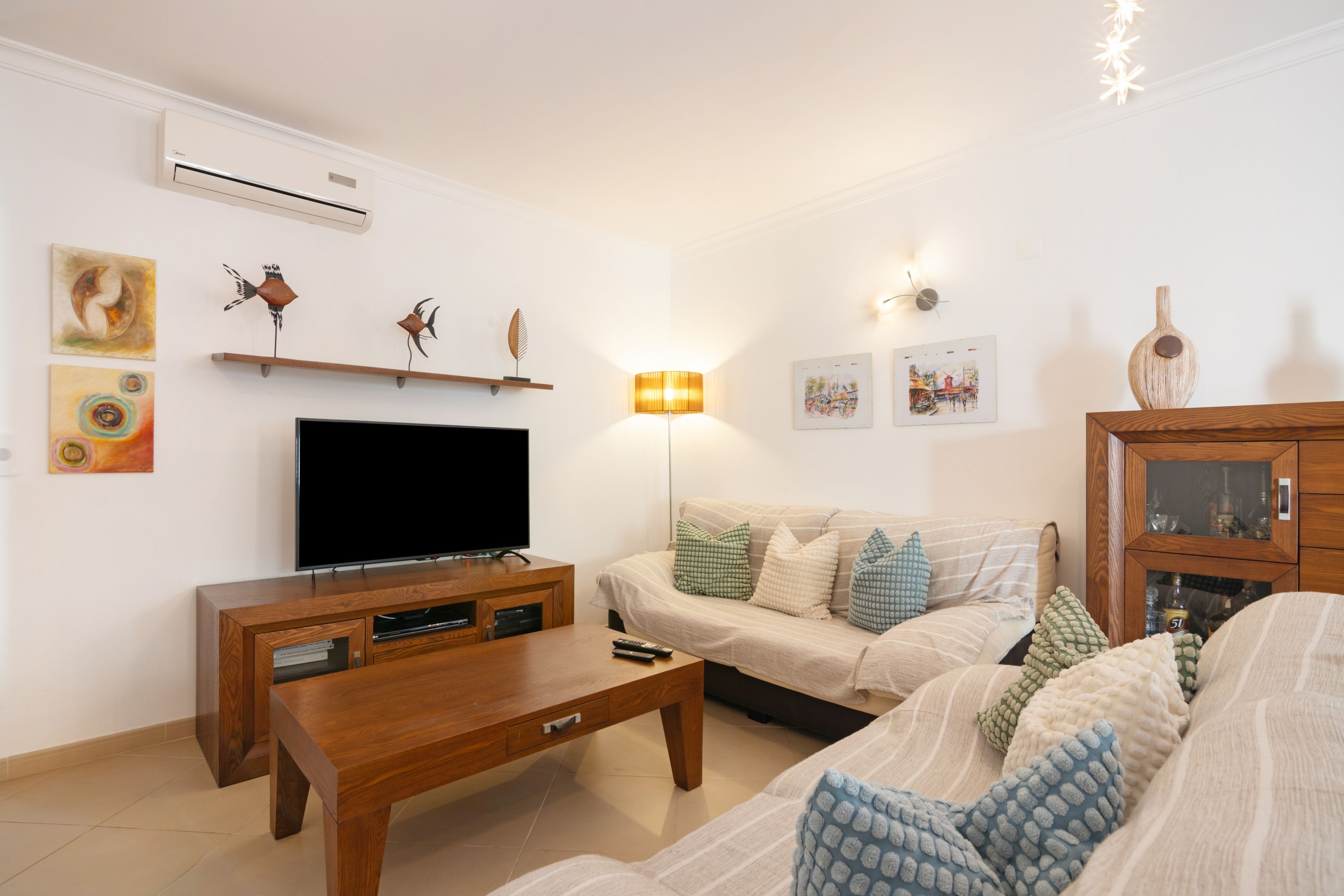Sala de estar con televisor de pantalla plana, mesa de centro de madera, sofá con cojines estampados y obra de arte en la pared.