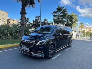 A black minivan parked on a street with palm trees and buildings in the background. - otel (Ankara)