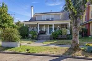 A two-story house with a front porch, a chimney, and a small front yard with a tree and a bench. - Hollywood District Duplex | Walk to MAX & Theatre (Portland)