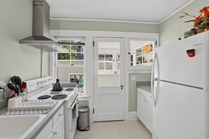 Cozinha compacta com eletrodomésticos brancos, coifa de aço inoxidável e janela com vista para o exterior.