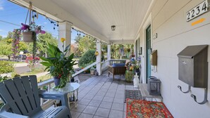 Une véranda couverte avec des meubles d’extérieur, des plantes en pot et une vue sur la rue.