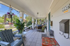 A covered porch with outdoor seating, potted plants, and a view of the street. - Hollywood District Duplex | Walk to MAX & Theatre (Portland)
