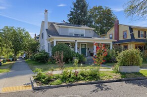 Uma casa de dois andares com varanda frontal, entrada por automóvel e um jardim bem cuidado.
