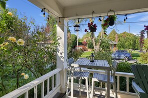 A covered porch with a table and chairs, surrounded by greenery and flowers. - Hollywood District Duplex | Walk to MAX & Theatre (Portland)