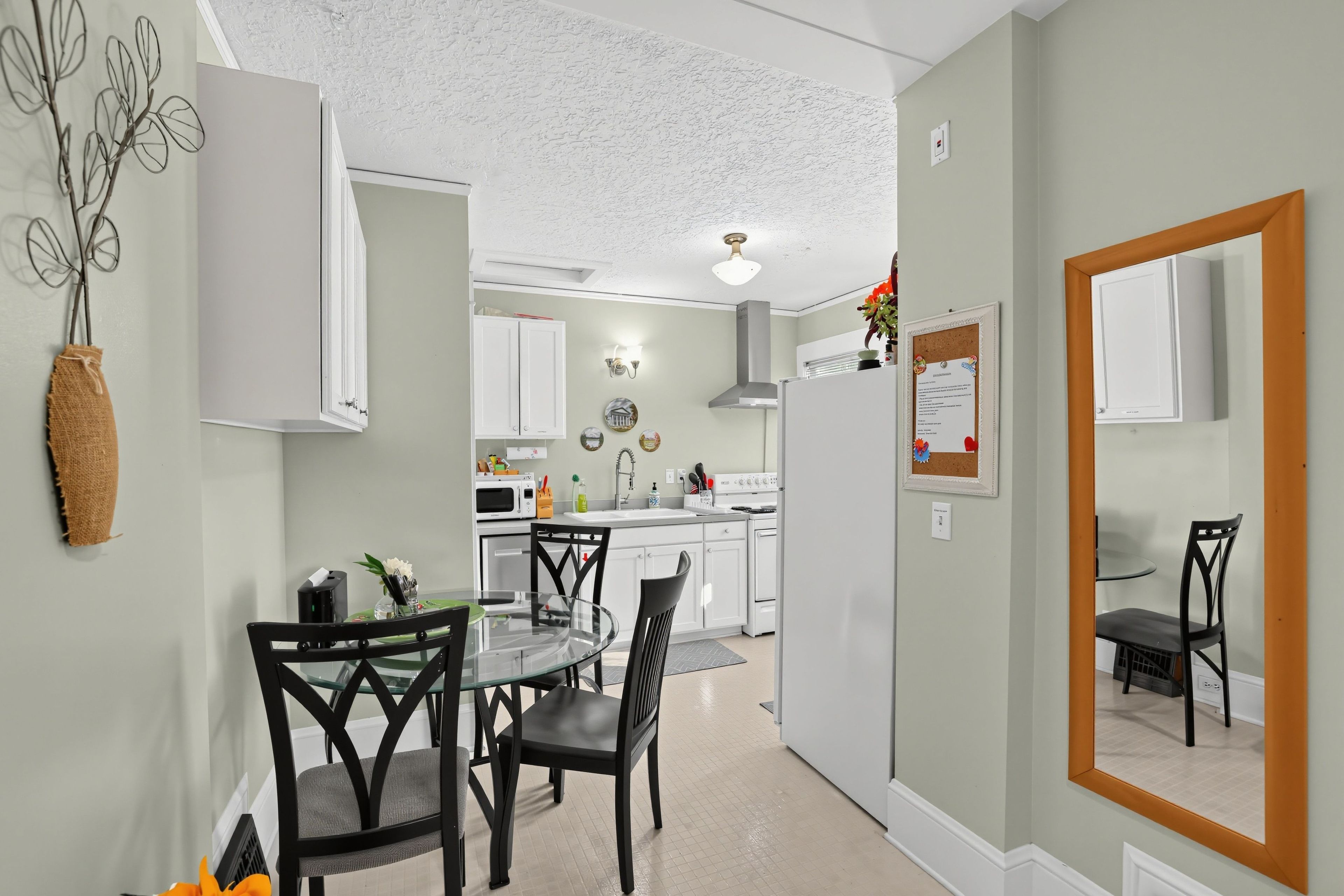 A modern kitchen with white cabinets, a dining area with a glass table and black chairs, and a large mirror on the wall.