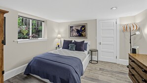 Une chambre à coucher avec un lit, une fenêtre ornée de plantes, une porte et une lampe.