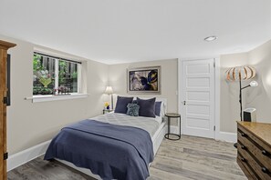 A bedroom with a bed, a window with plants, a door, and a lamp. - Hollywood District Duplex | Walk to MAX & Theatre (Portland)