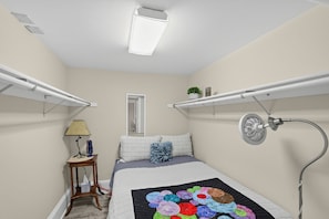Quarto com cama, mesa de cabeceira com luminária, radiador e janela.
