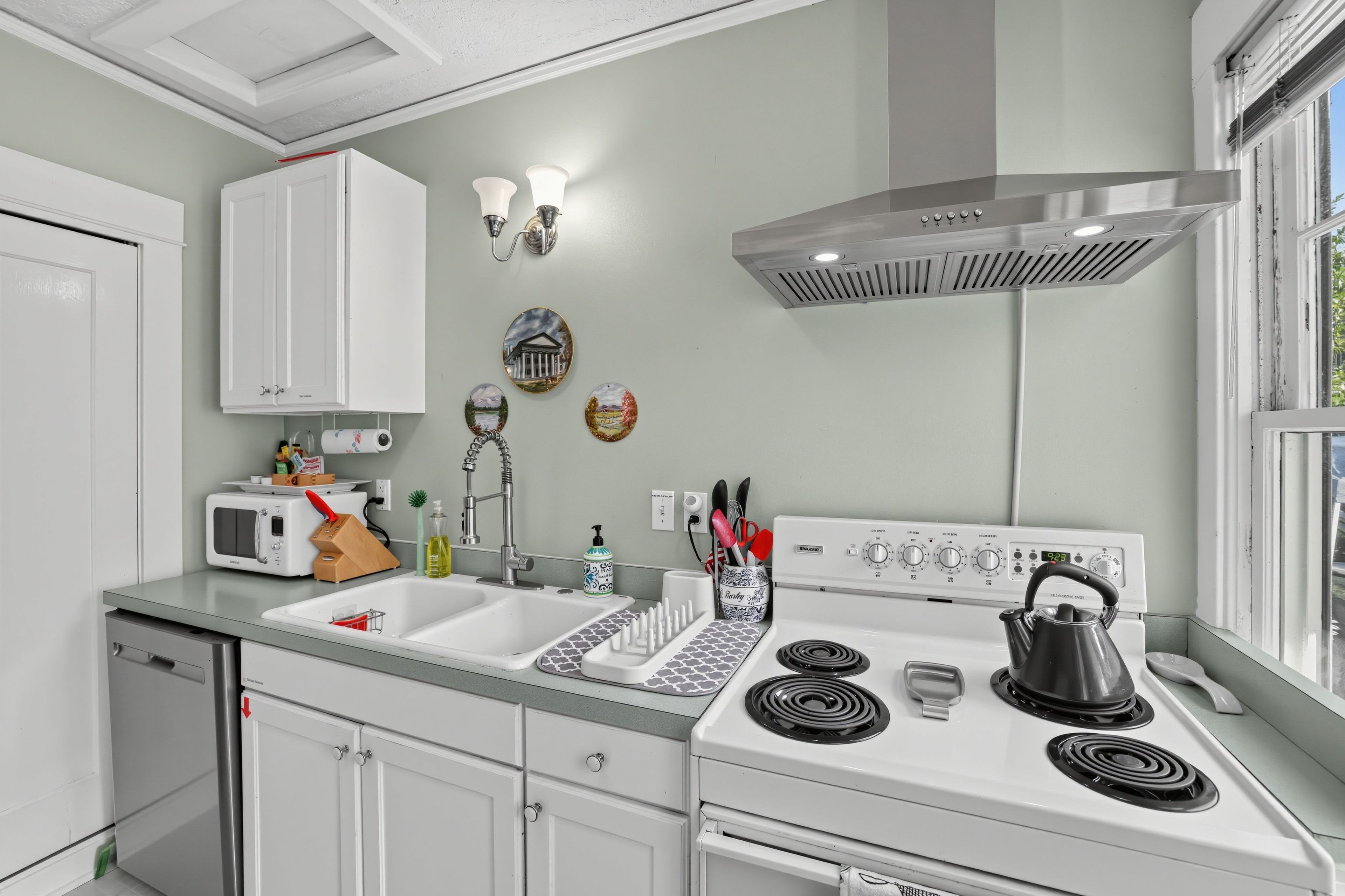 A kitchen with white cabinets, a stove, a microwave, and a sink.
