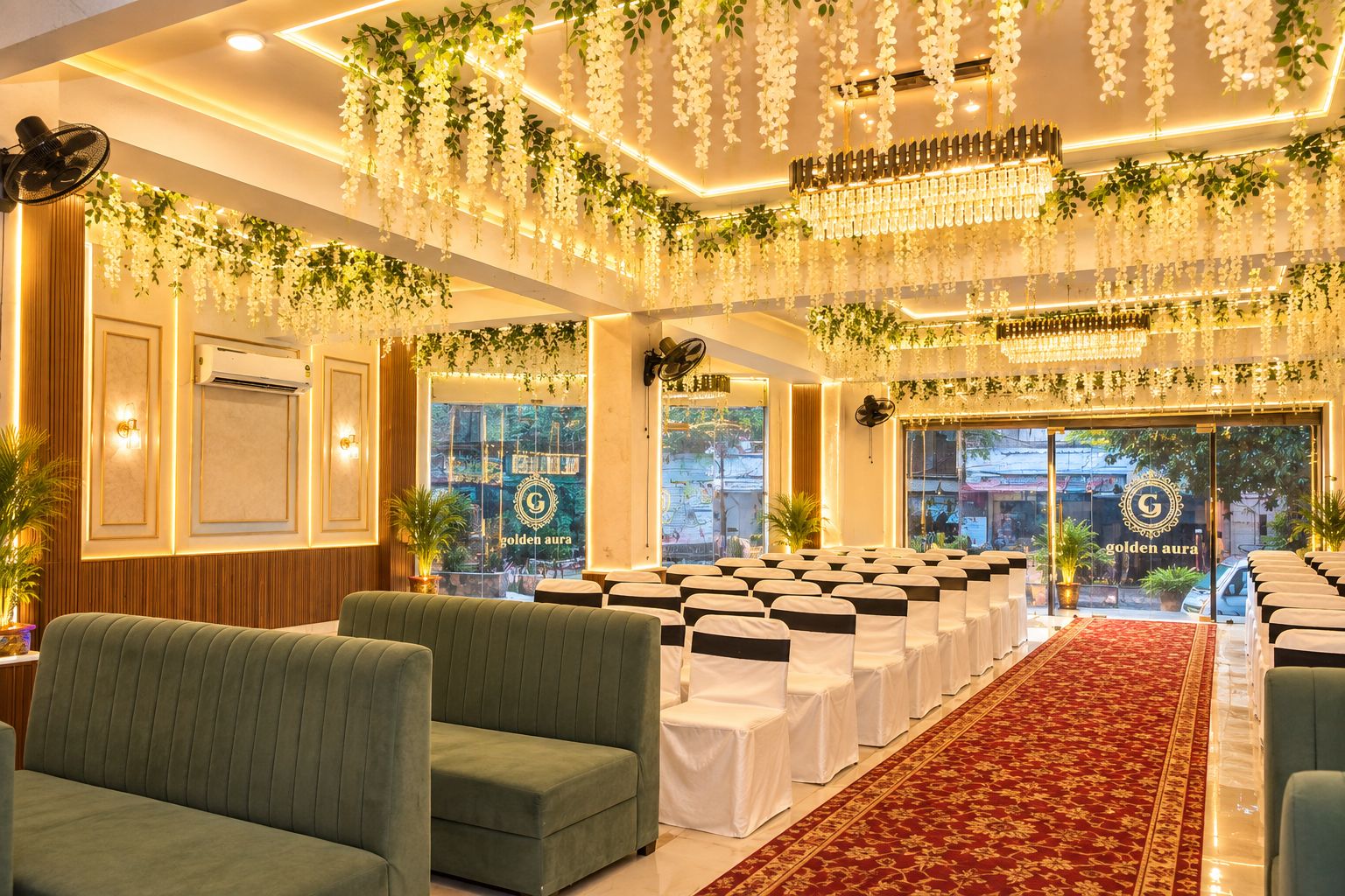 A banquet hall with rows of white chairs, a red carpet, and hanging floral decorations.