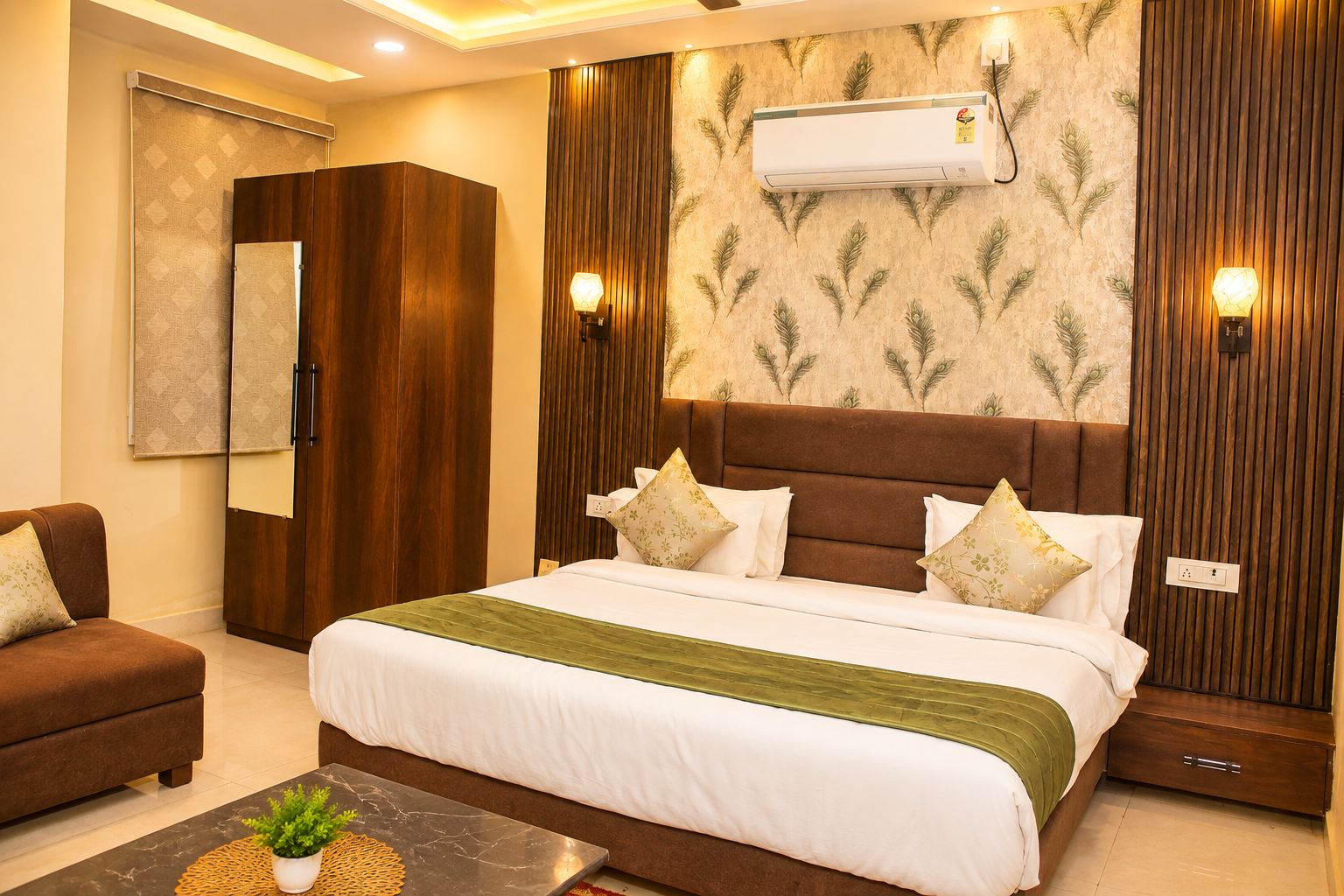 A hotel room with a large bed, a wardrobe, a seating area, and an air conditioning unit on the wall.