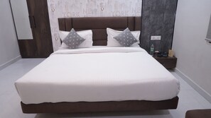 A large bed with a brown headboard, white bedding, and two pillows with gray polka dots. - Hotel Golden Aura Inn (Gwalior)