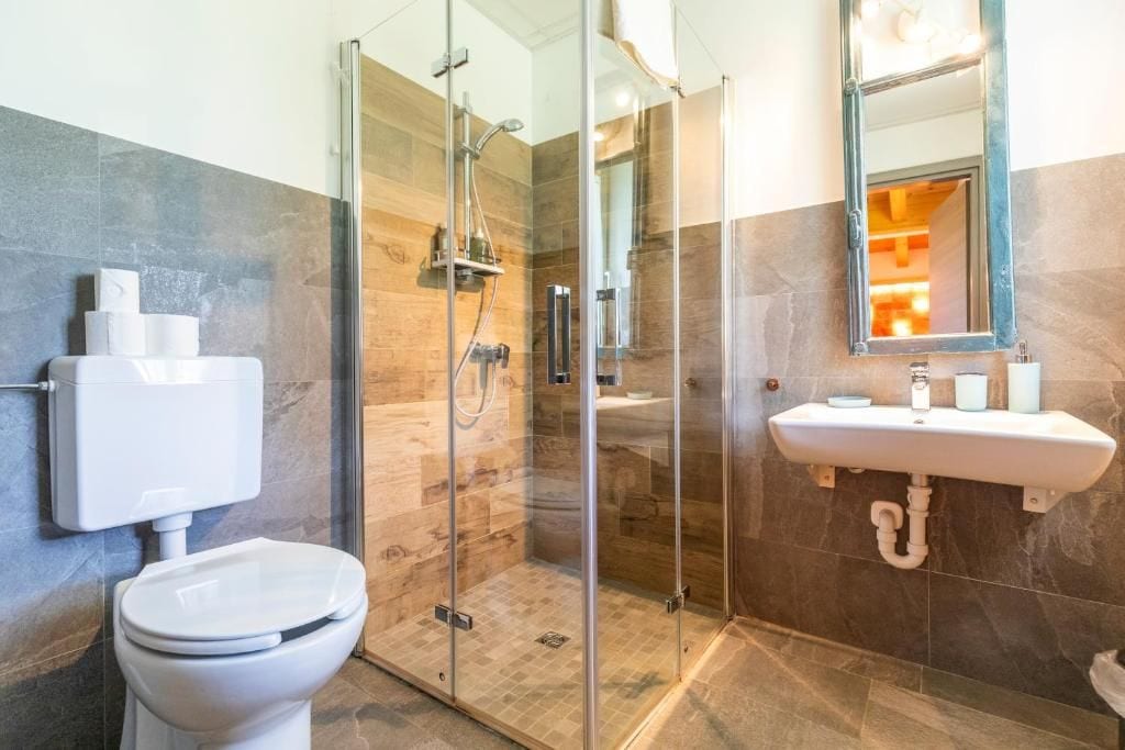 Ein modernes Badezimmer mit einer Duschkabine, einer Toilette und einem Waschbecken mit Spiegel darüber.