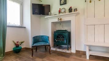 Una habitación con chimenea, un televisor montado sobre ella, un sillón azul y suelo de madera.