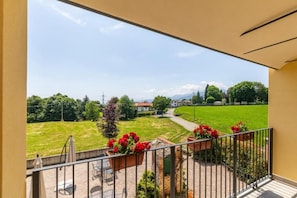 A balcony with a view of a green field and houses in the distance.