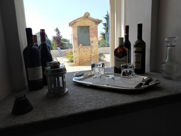 A kitchen counter with wine bottles, a tray with glasses, and a view of a brick building outside.