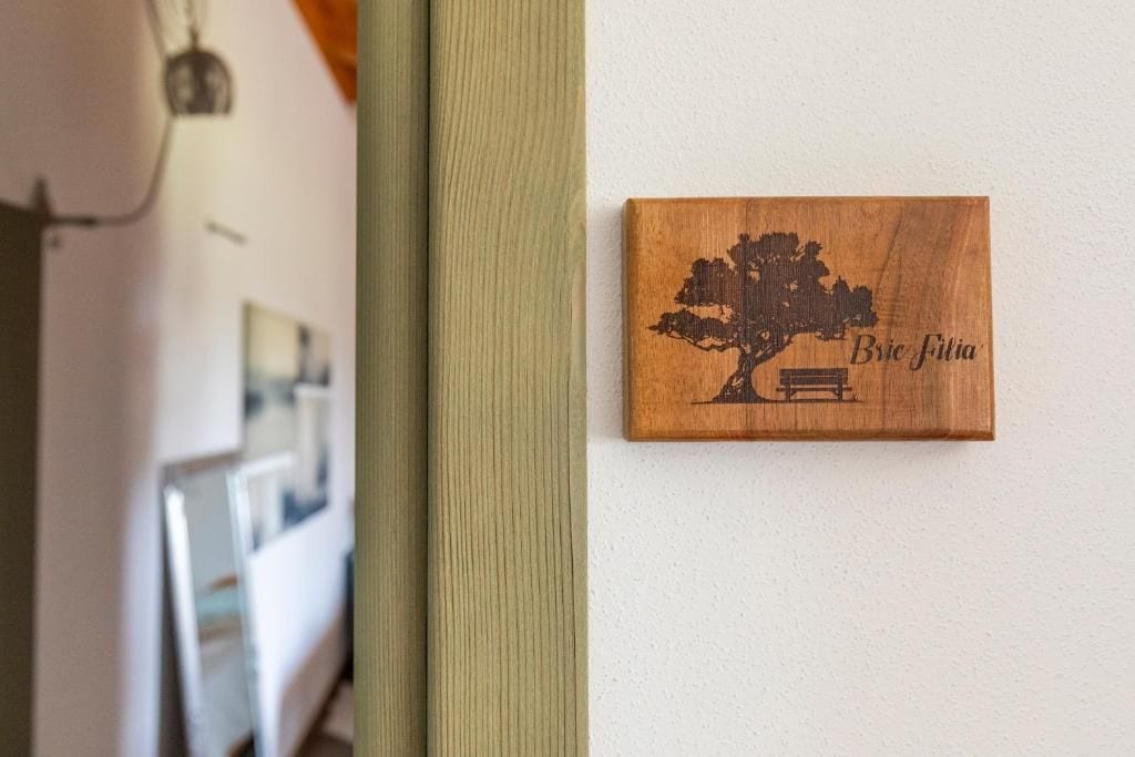 A wooden plaque with a tree and bench design, labeled 'Bric Filia,' mounted on a wall.