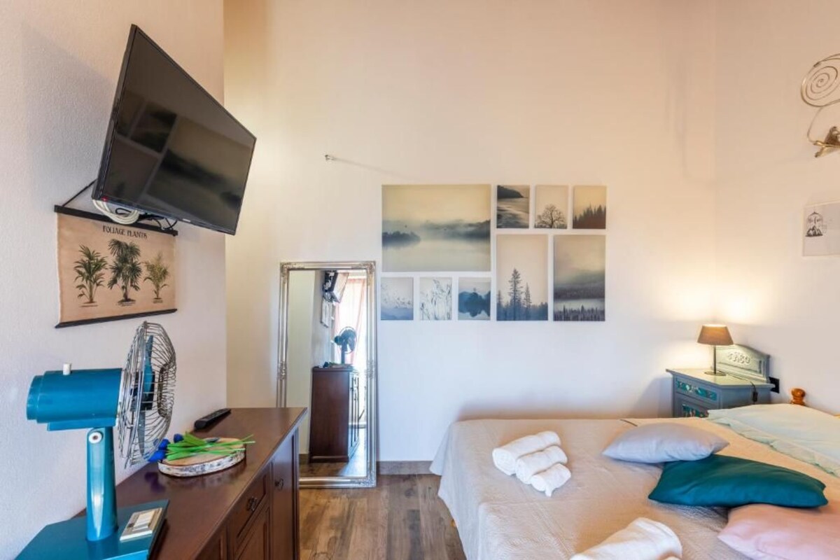 Une chambre à coucher comprenant un lit, un téléviseur fixé au mur, un ventilateur, une commode et un miroir.