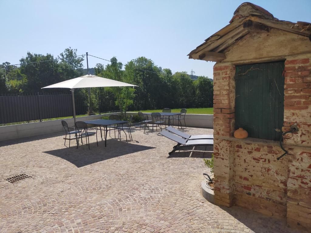 Ein Außenbereich mit einer Ziegelterrasse, einem Tisch mit Stühlen, einem Sonnenschirm und einem kleinen Backsteinhaus mit einer grünen Tür.