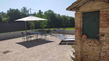 Ein Außenbereich mit einer Ziegelterrasse, einem Tisch mit Stühlen, einem Sonnenschirm und einem kleinen Backsteinhaus mit einer grünen Tür.