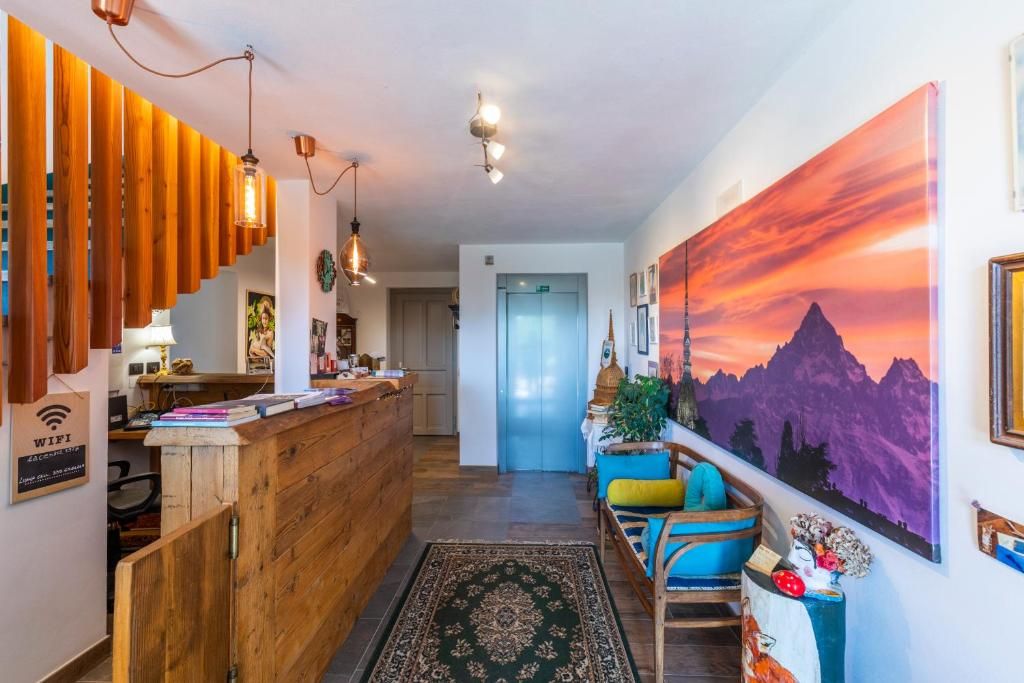 A hotel lobby with a wooden reception desk, a large painting of a mountain landscape, and a staircase leading to the upper floors.