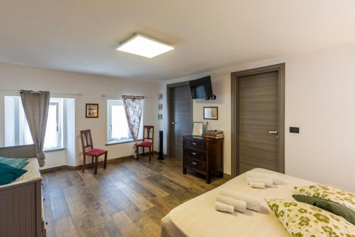 Une chambre à coucher comprenant un lit, une commode, une chaise, un bureau, un téléviseur et une porte.