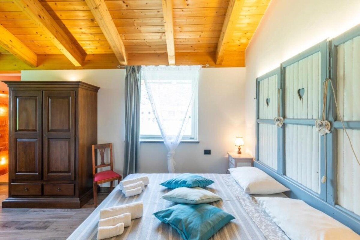 Une chambre avec un plafond en bois, une grande armoire, un lit avec des oreillers et une fenêtre avec des rideaux.