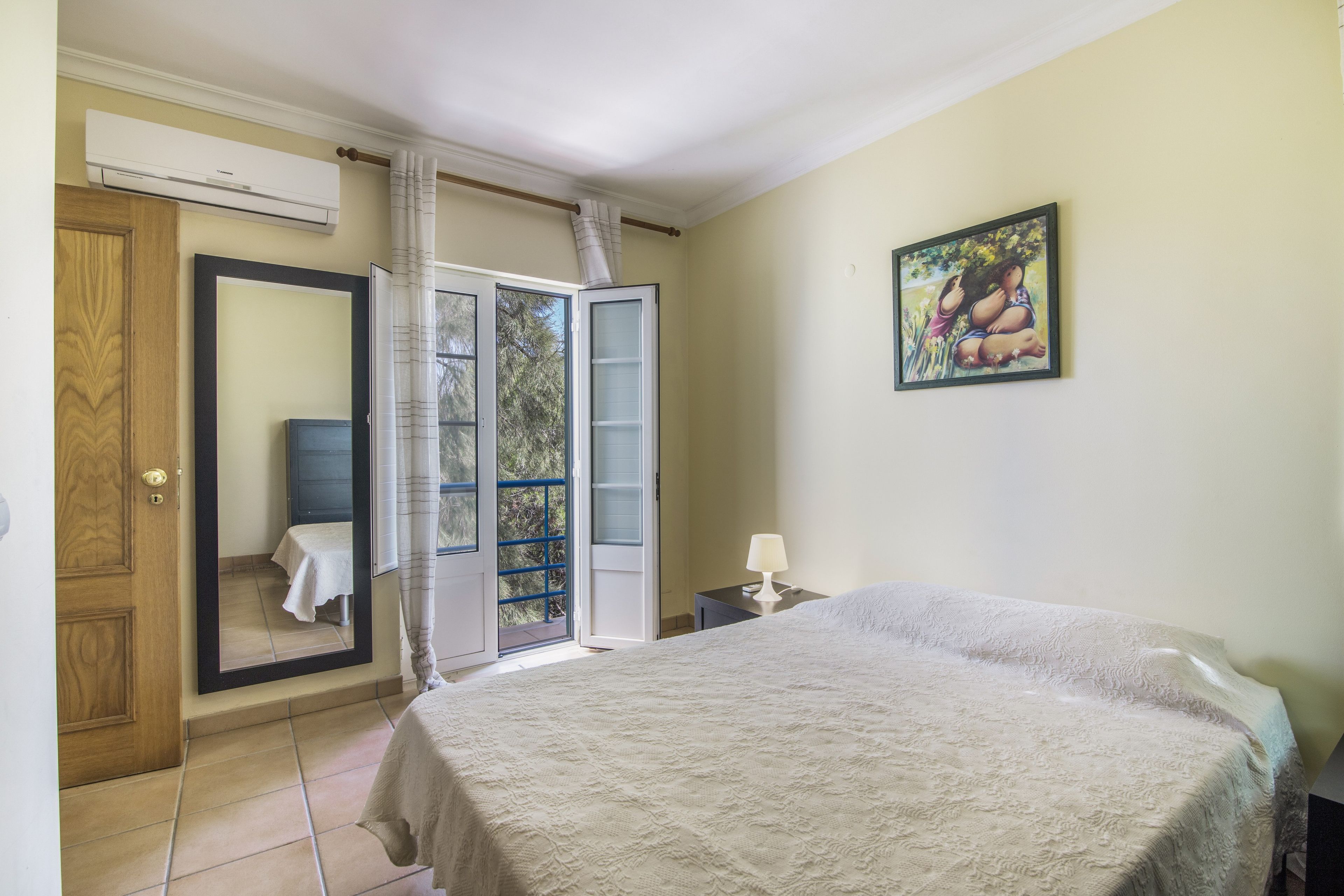 Une chambre à coucher comprenant un lit, une table de chevet, une lampe, un tableau, une armoire et une salle de bain avec un rideau de douche.