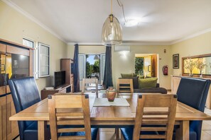 Un comedor con una mesa y sillas de madera, un televisor y vistas al exterior.