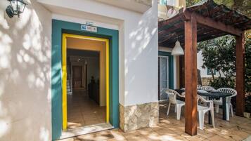 A building entrance with a sign 'LOTE 3-B', a covered outdoor seating area with tables and chairs, and a tiled patio.