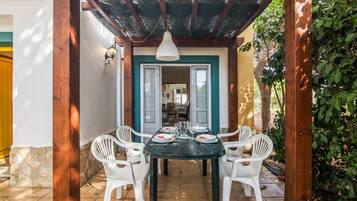 Een terras buiten met een tafel voor vier personen, omringd door witte stoelen, onder een houten pergola.