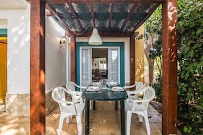 An outdoor patio with a table set for four, surrounded by white chairs, under a wooden pergola.