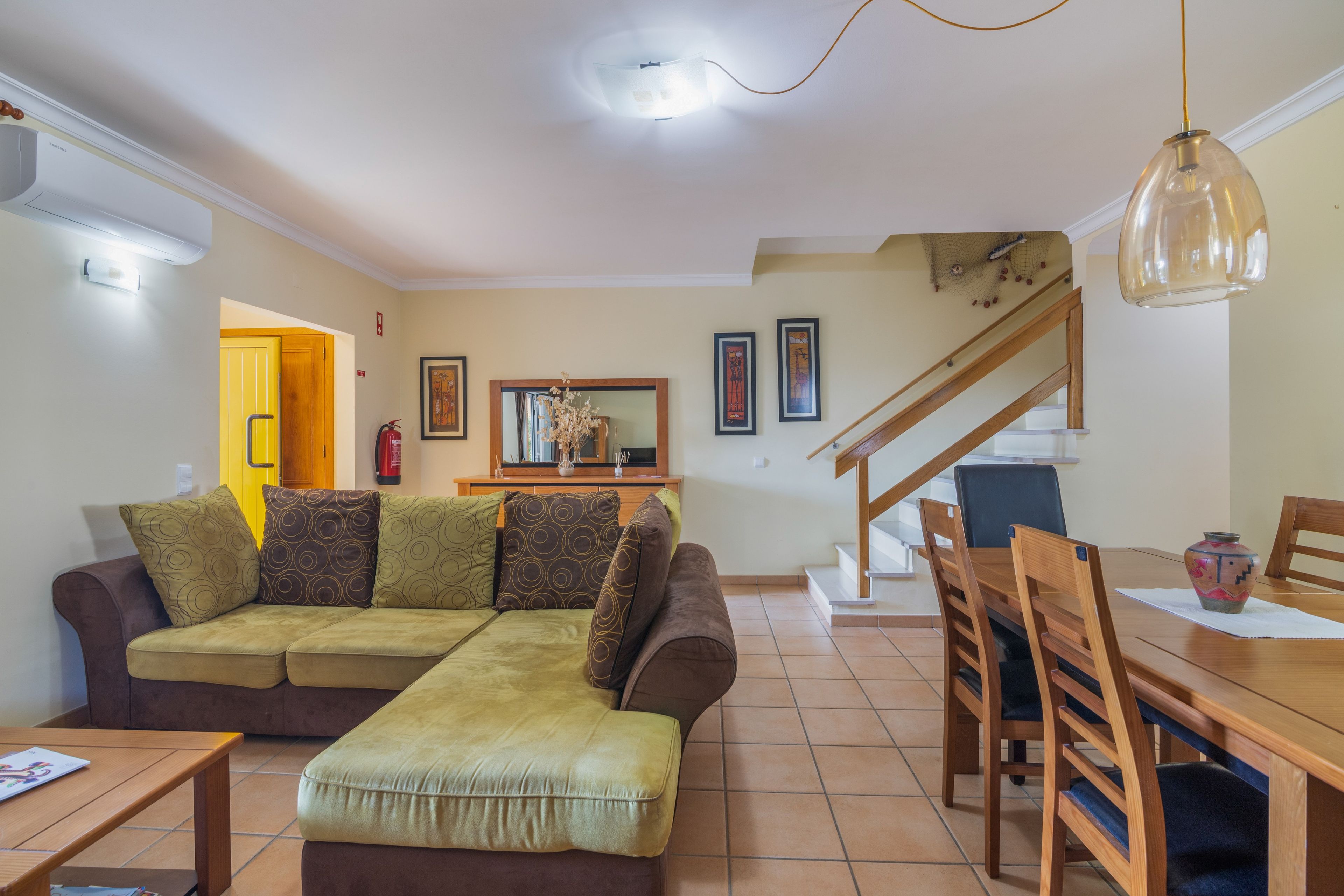 Un salon avec un canapé, une table à manger avec des chaises, un escalier et un couloir menant à une autre pièce.