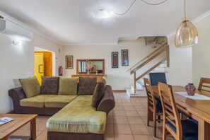 Una sala de estar con un sofá, una mesa de comedor con sillas, una escalera y un pasillo que conduce a otra habitación.