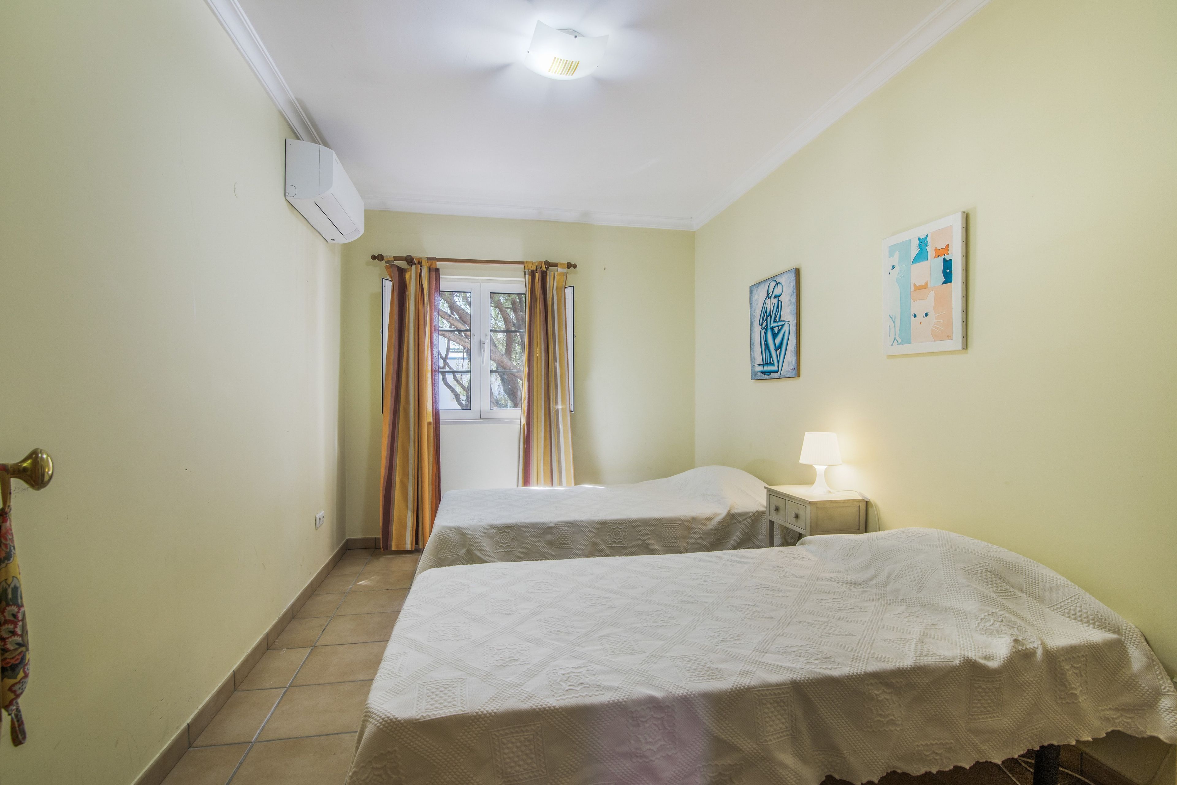 Una habitación con dos camas, una ventana con cortinas, aire acondicionado instalado en la pared y un cuadro.