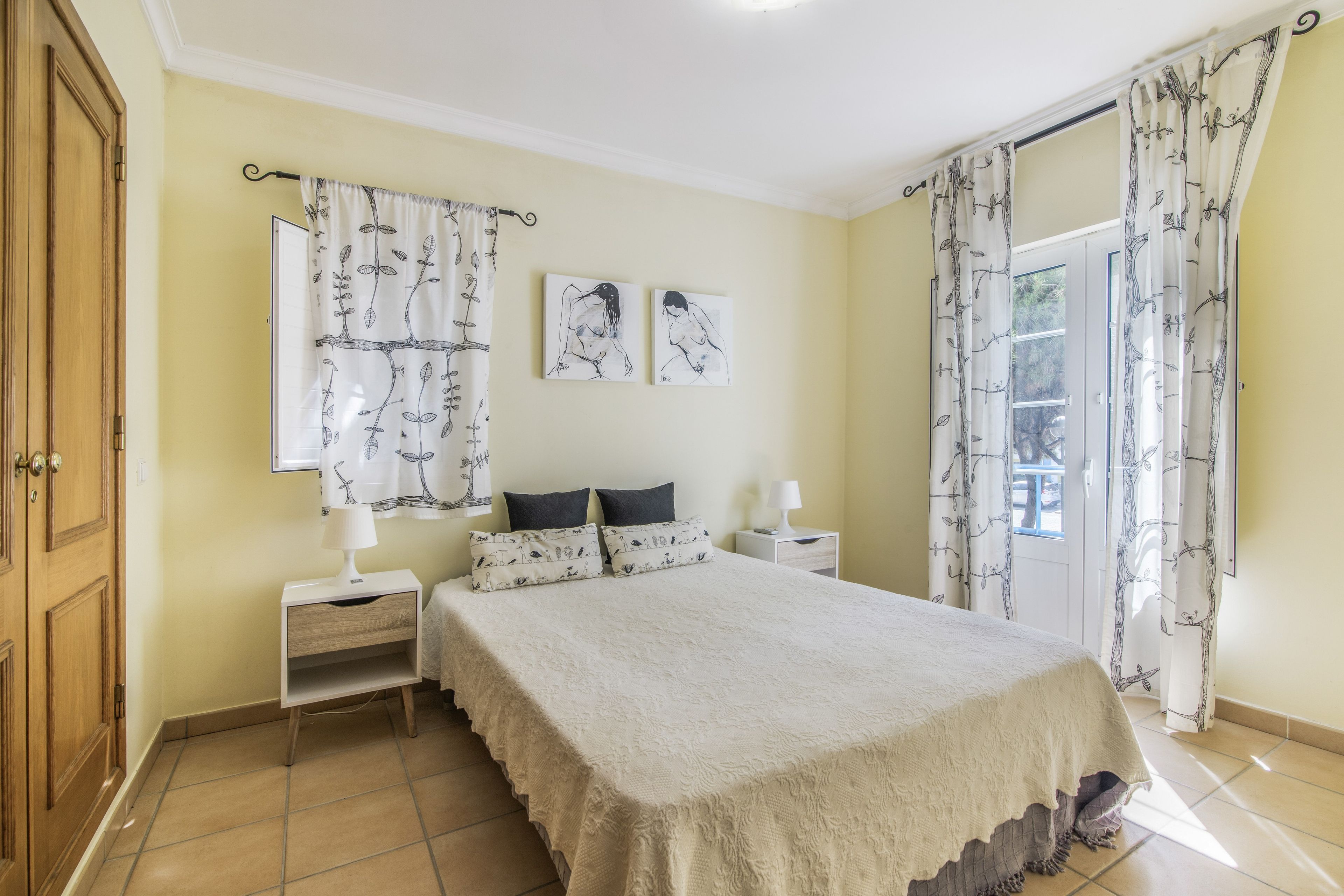 Un dormitorio con cama, dos mesitas de noche, una ventana con cortinas y una obra de arte en la pared.