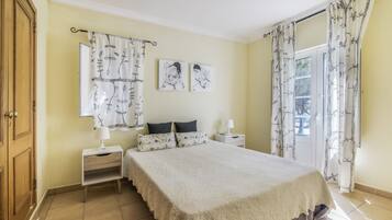 Un dormitorio con cama, dos mesitas de noche, una ventana con cortinas y una obra de arte en la pared.
