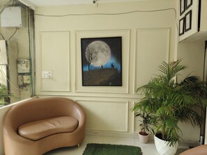 A living room with a framed artwork of a tree and deer under a full moon, a brown leather sofa, and a potted plant. - Hotel Weekend by Benchmark (Indore)