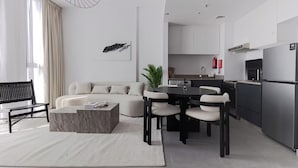 En moderne stue med sofa, sofabord og spiseplads. Der er et køkken med køleskab og mikrobølgeovn.