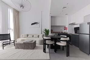 Een moderne woonkamer met een bank, salontafel en eethoek. Er is een keuken met een koelkast en magnetron.