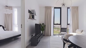 Et moderne hotelværelse med seng, siddeområde med bord, fjernsyn og en balkon med udsigt.